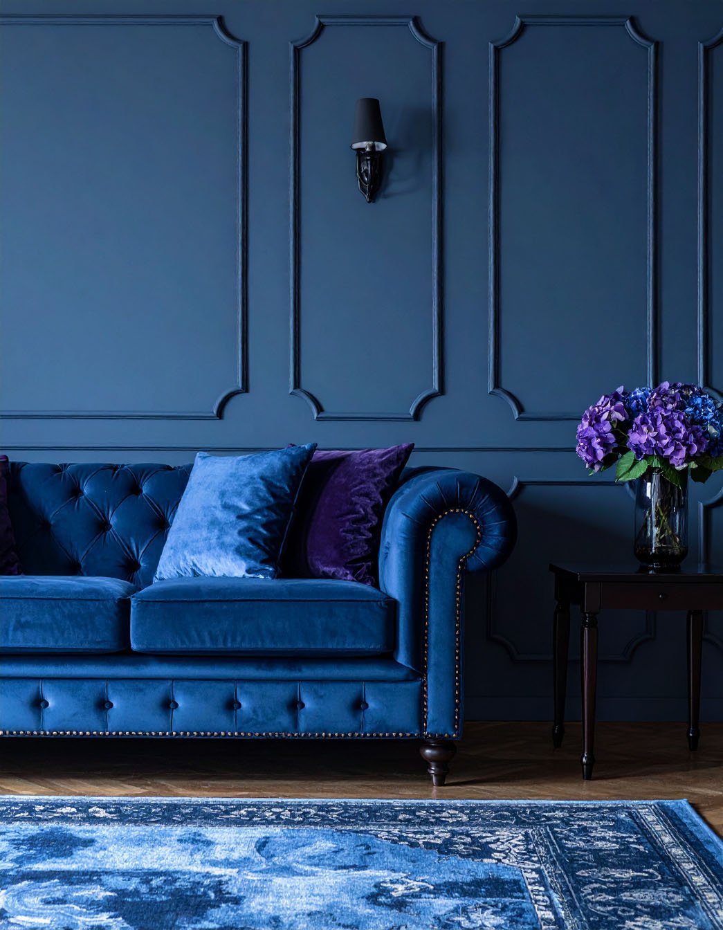 Salon avec murs gris, canapé Chesterfield en velours bleu et tapis à motifs