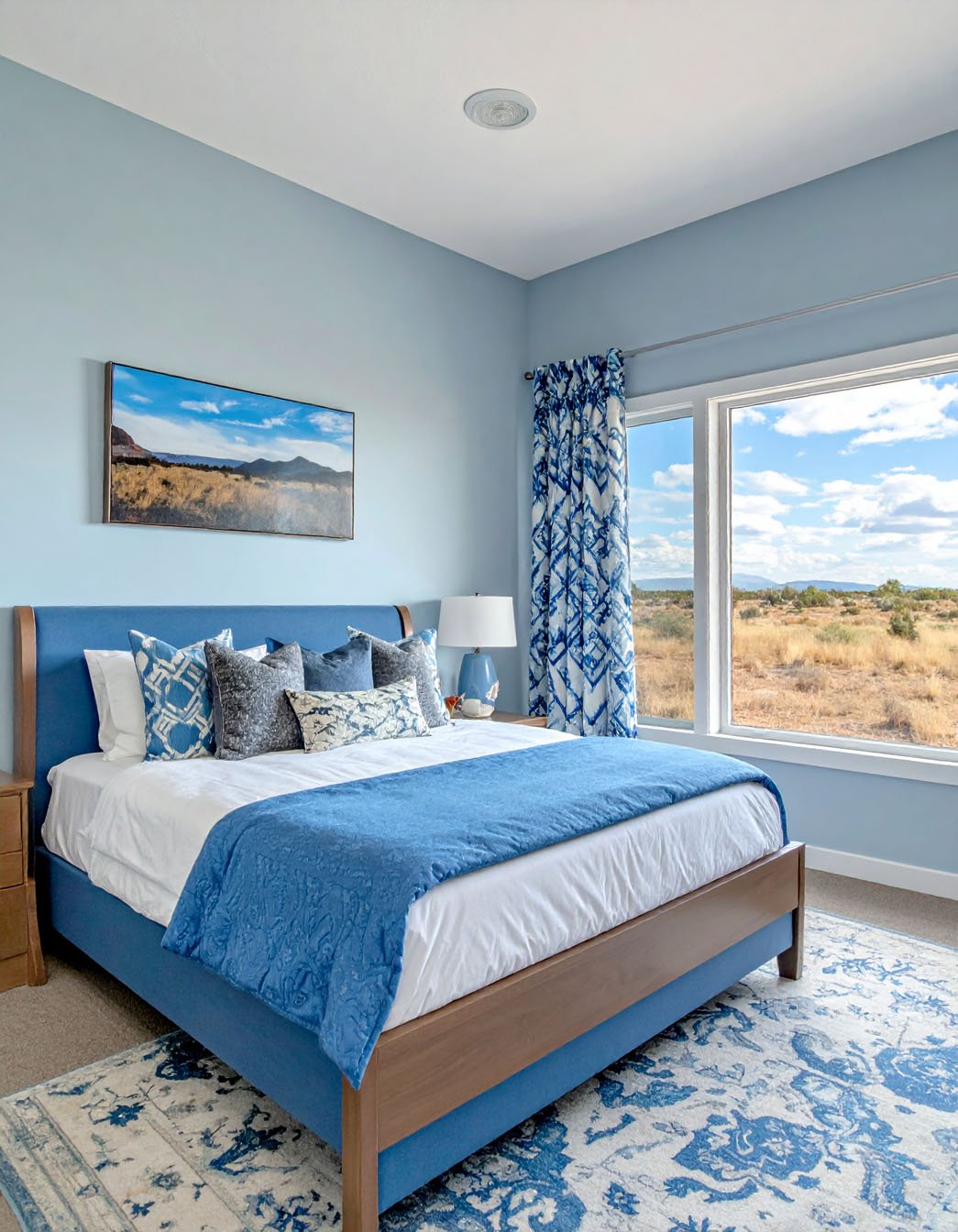 Chambre avec murs bleus, lit en bois, parure à motifs et tapis coloré