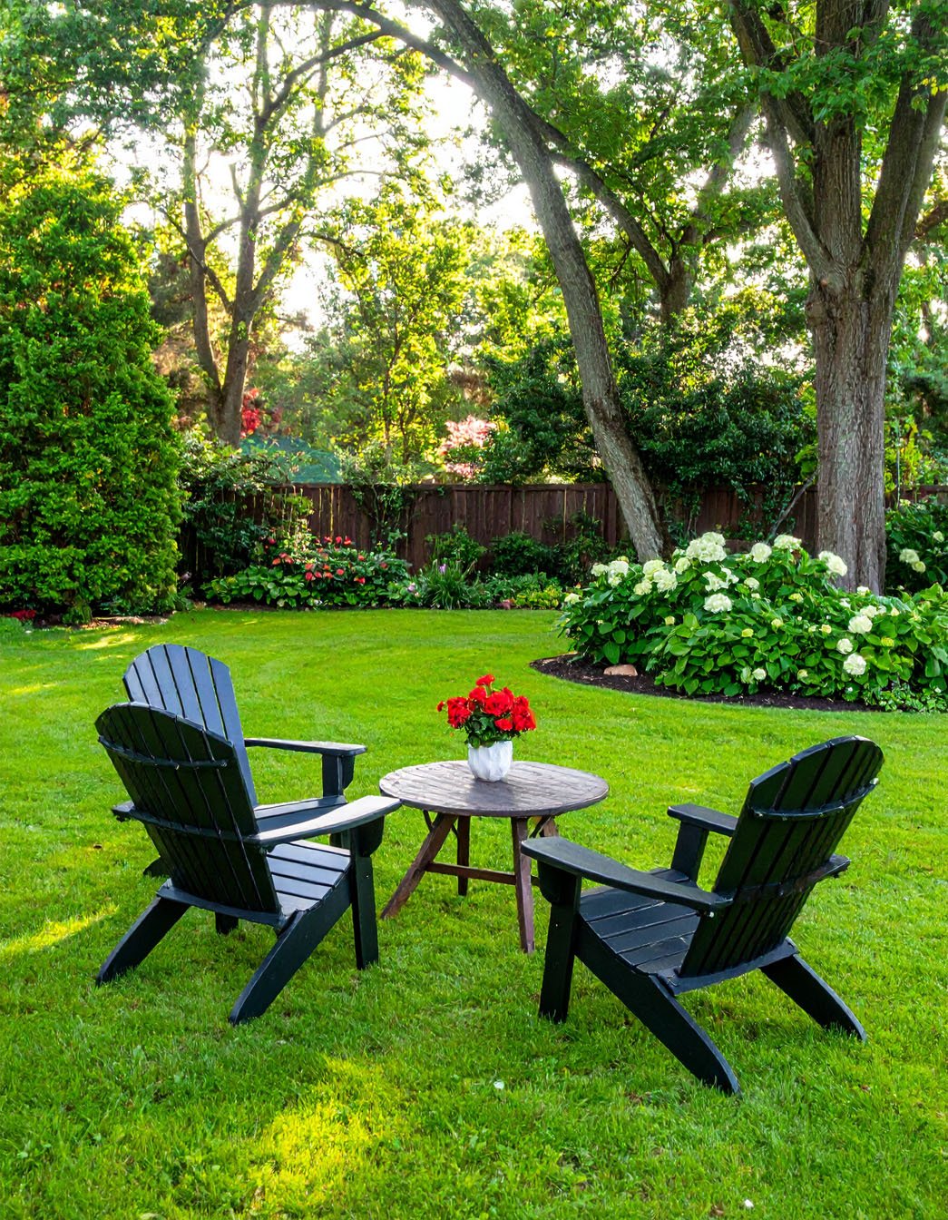 Deux fauteuils Adirondack noirs sur une pelouse verdoyante avec table et fleurs rouges