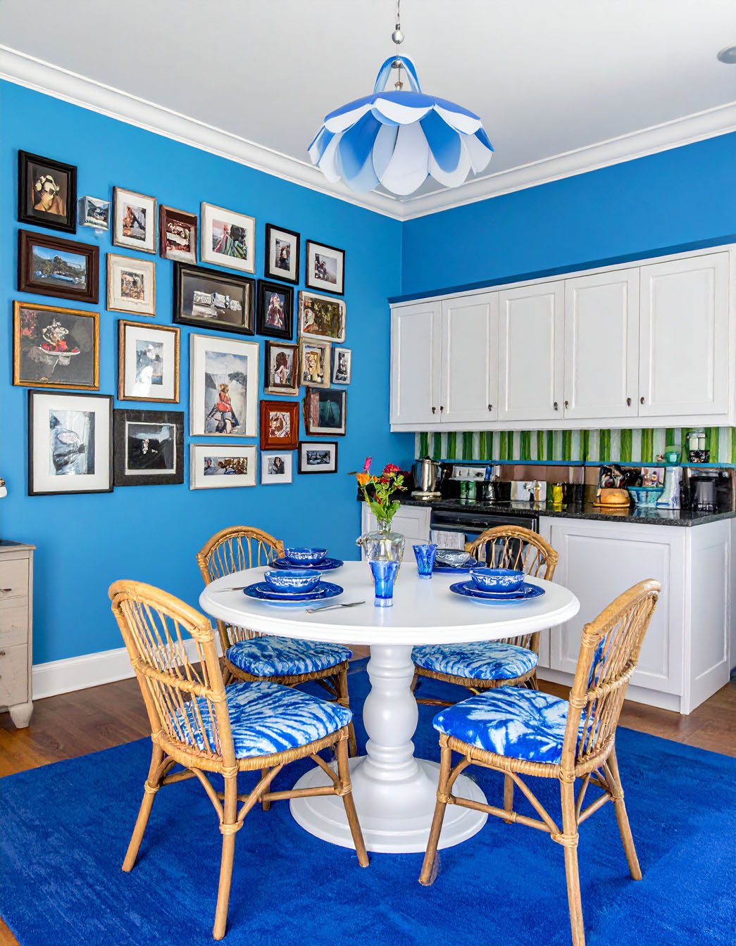 Salle à manger avec murs bleus vifs, table blanche, chaises en rotin et mur de cadres