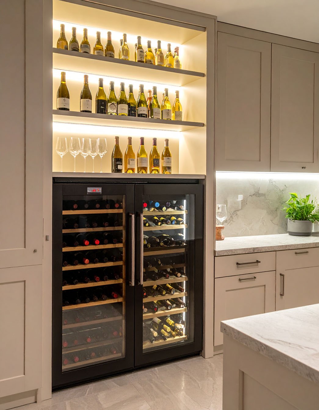 Cave à vin intégrée avec étagères lumineuses remplies de bouteilles, à côté de meubles de cuisine clairs
