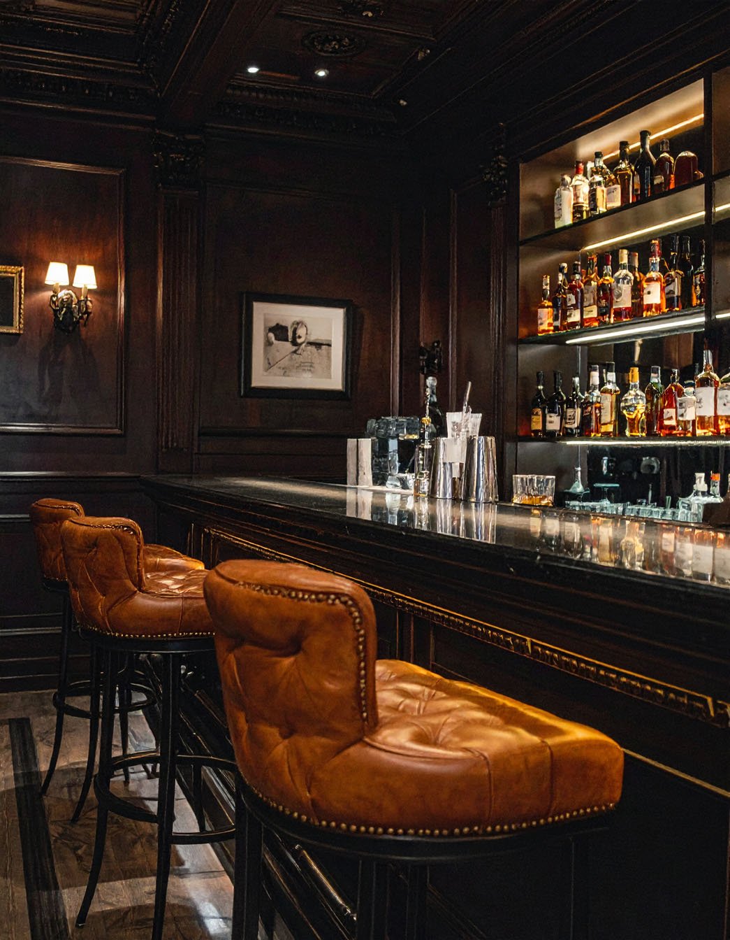 Bar sombre et luxueux avec boiseries, comptoir en marbre et tabourets en cuir marron