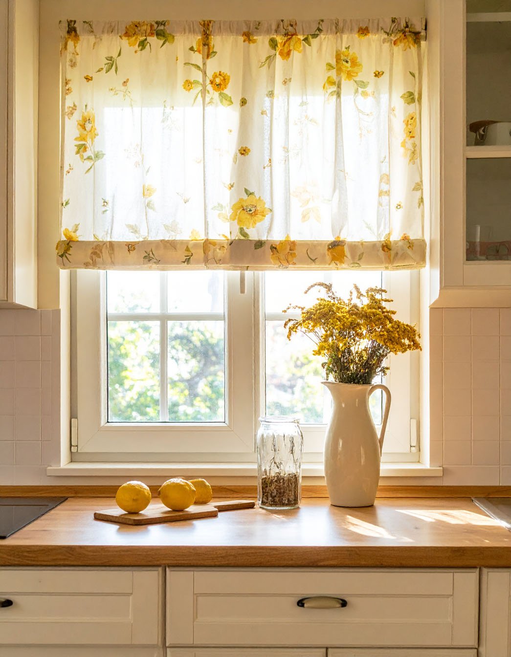 Fenêtre de cuisine avec rideau à fleurs jaunes, citrons et pichet de fleurs séchées