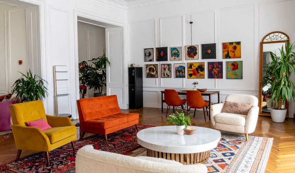Salon éclectique avec murs blancs, parquet à chevrons, canapés et fauteuils colorés, tapis orientaux