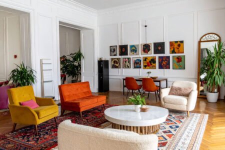 Salon éclectique avec murs blancs, parquet à chevrons, canapés et fauteuils colorés, tapis orientaux