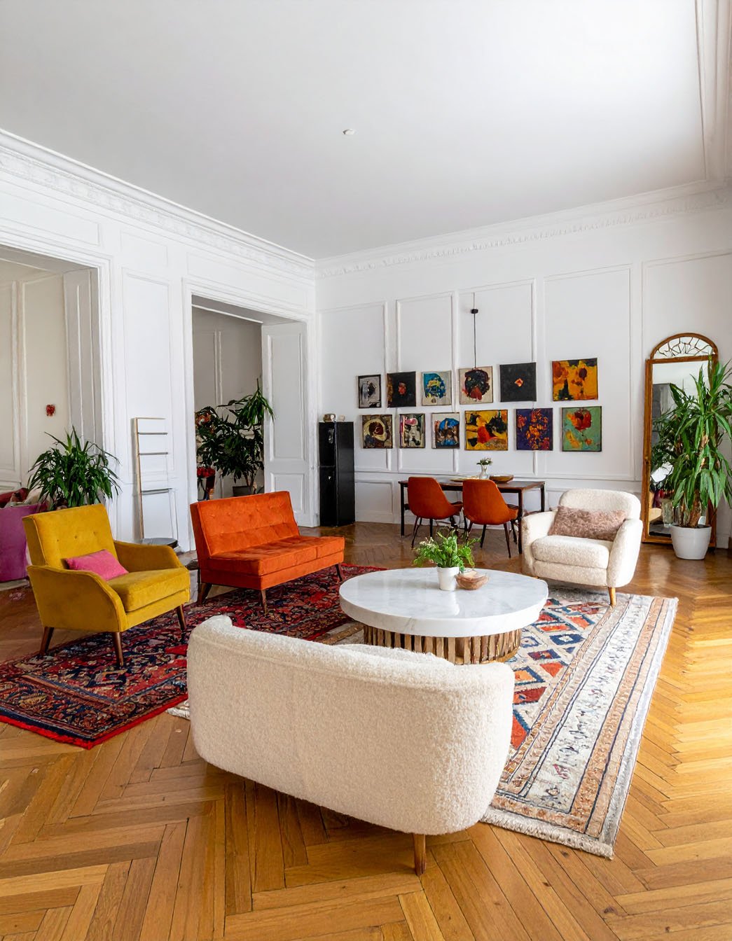 Salon éclectique avec murs blancs, parquet à chevrons, canapés et fauteuils colorés, tapis orientaux
