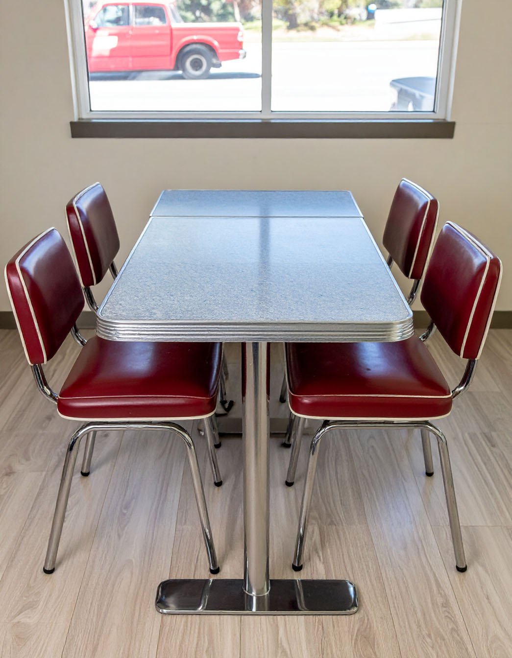 Table de diner rétro avec chaises rouges et bordures chromées devant une fenêtre