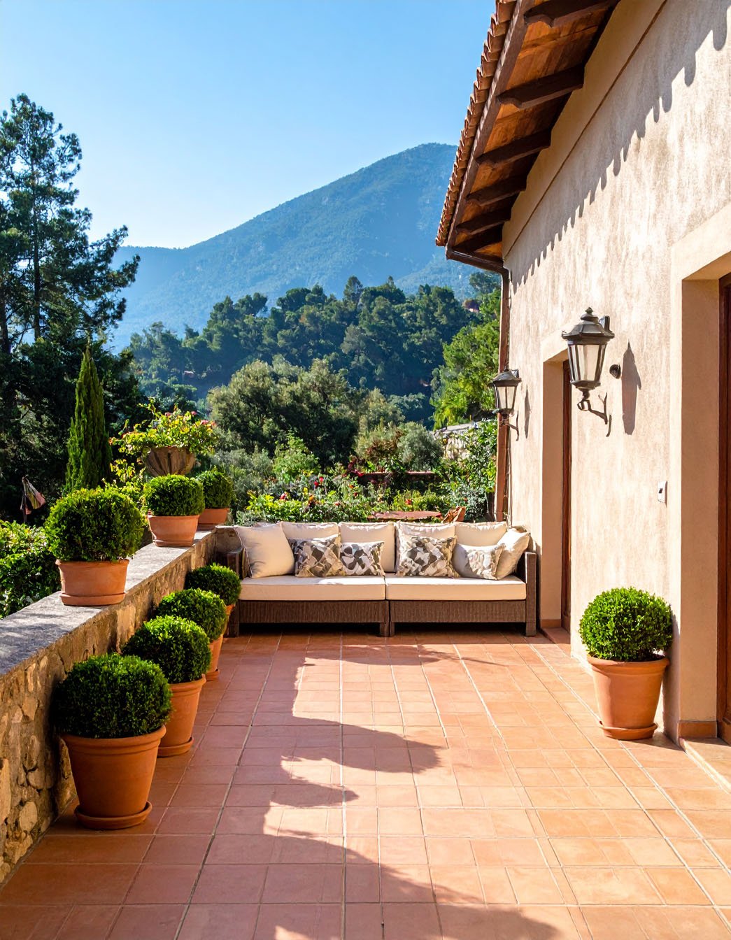 Terrasse en terre cuite avec canapé, buis en pots et vue sur des montagnes boisées