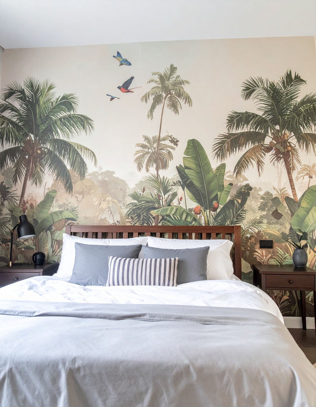 Chambre avec lit en bois foncé, literie grise et papier peint panoramique de jungle tropicale