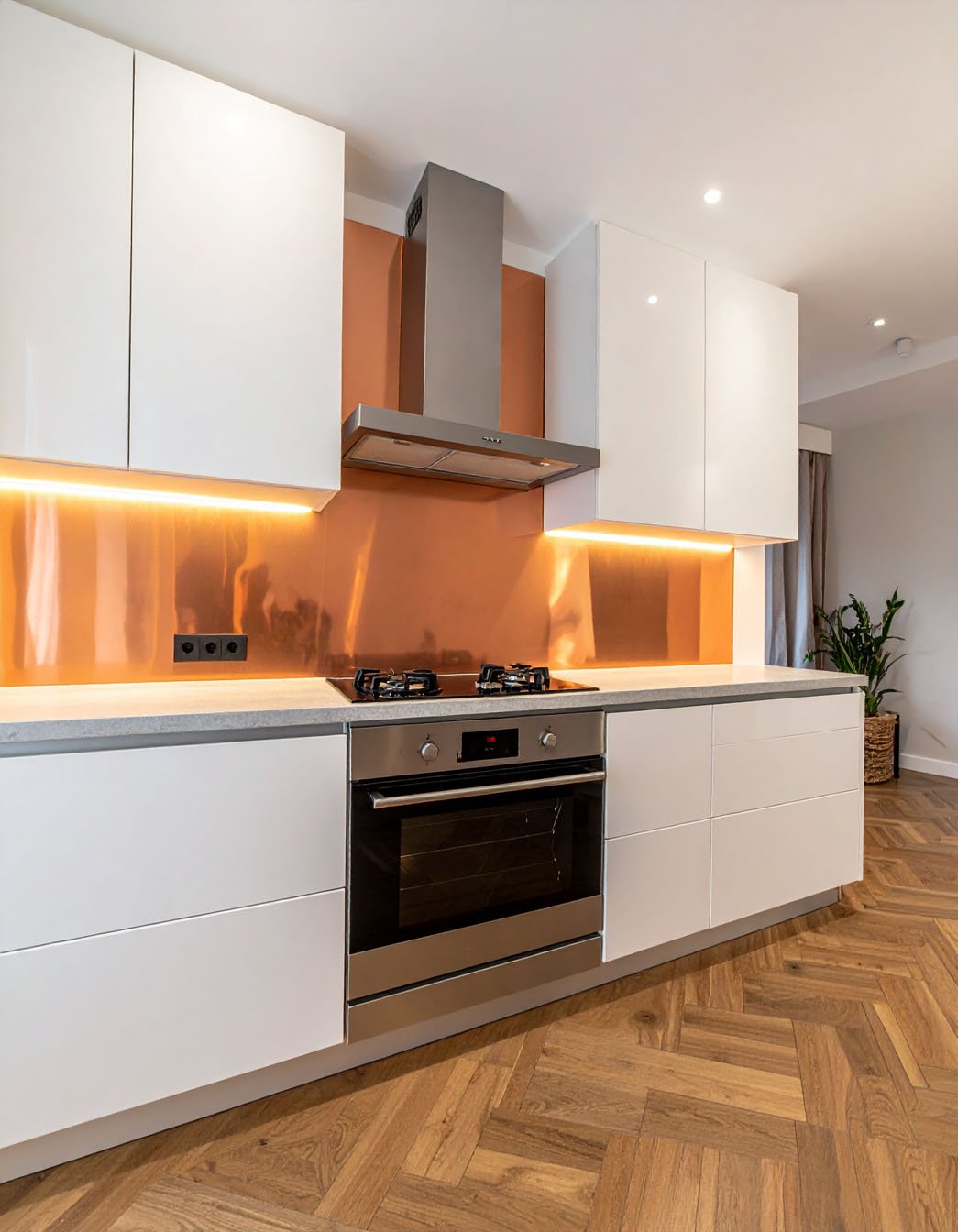Cuisine avec meubles blancs, crédence cuivrée brillante et parquet à chevrons