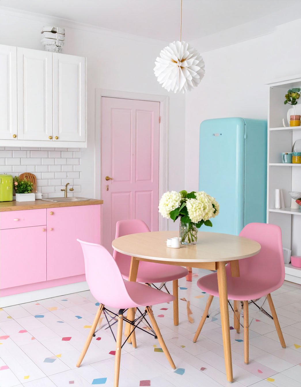Cuisine ludique avec meubles bas roses, réfrigérateur bleu pastel et table avec chaises roses