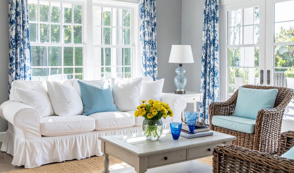 Salon lumineux avec canapé blanc, fauteuils en rotin et rideaux à motifs bleus et blancs