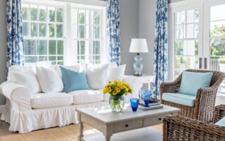 Salon lumineux avec canapé blanc, fauteuils en rotin et rideaux à motifs bleus et blancs