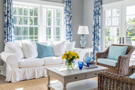 Salon lumineux avec canapé blanc, fauteuils en rotin et rideaux à motifs bleus et blancs