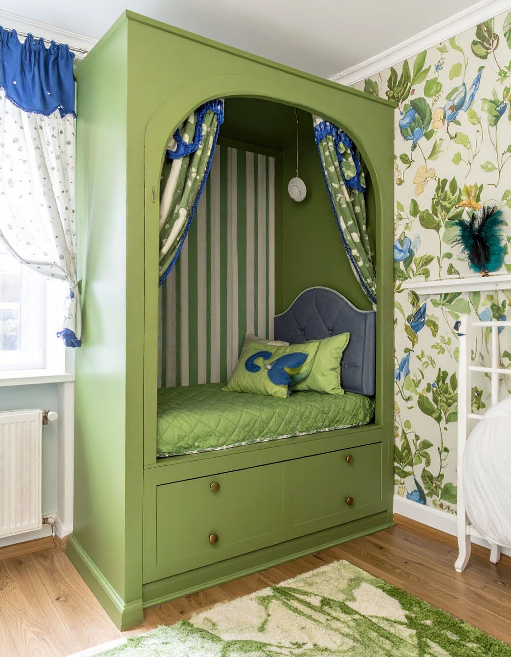 Lit d'enfant vert en alcôve avec rideaux rayés et papier peint floral