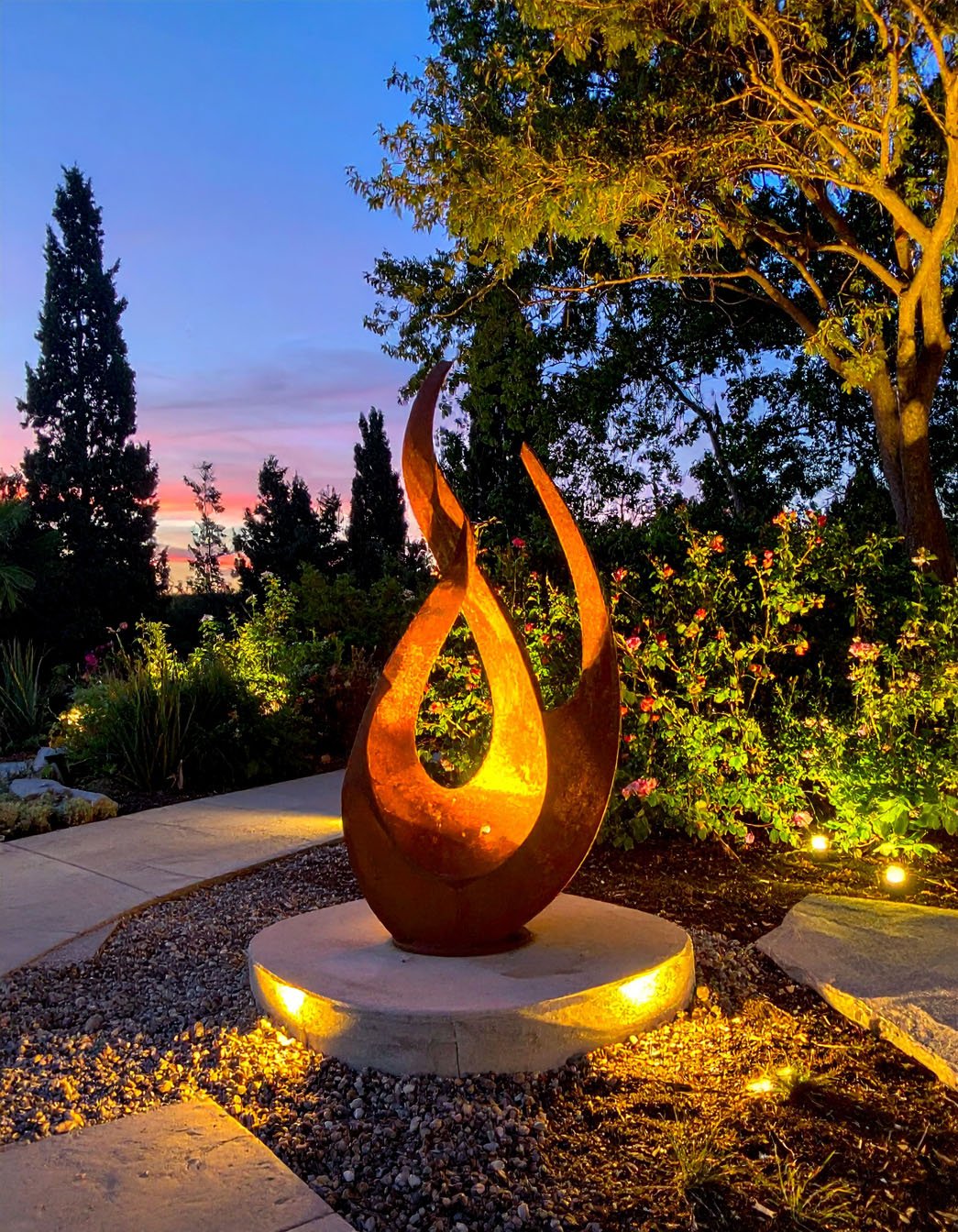 Sculpture de flamme en métal rouillé éclairée dans un jardin paysager au crépuscule
