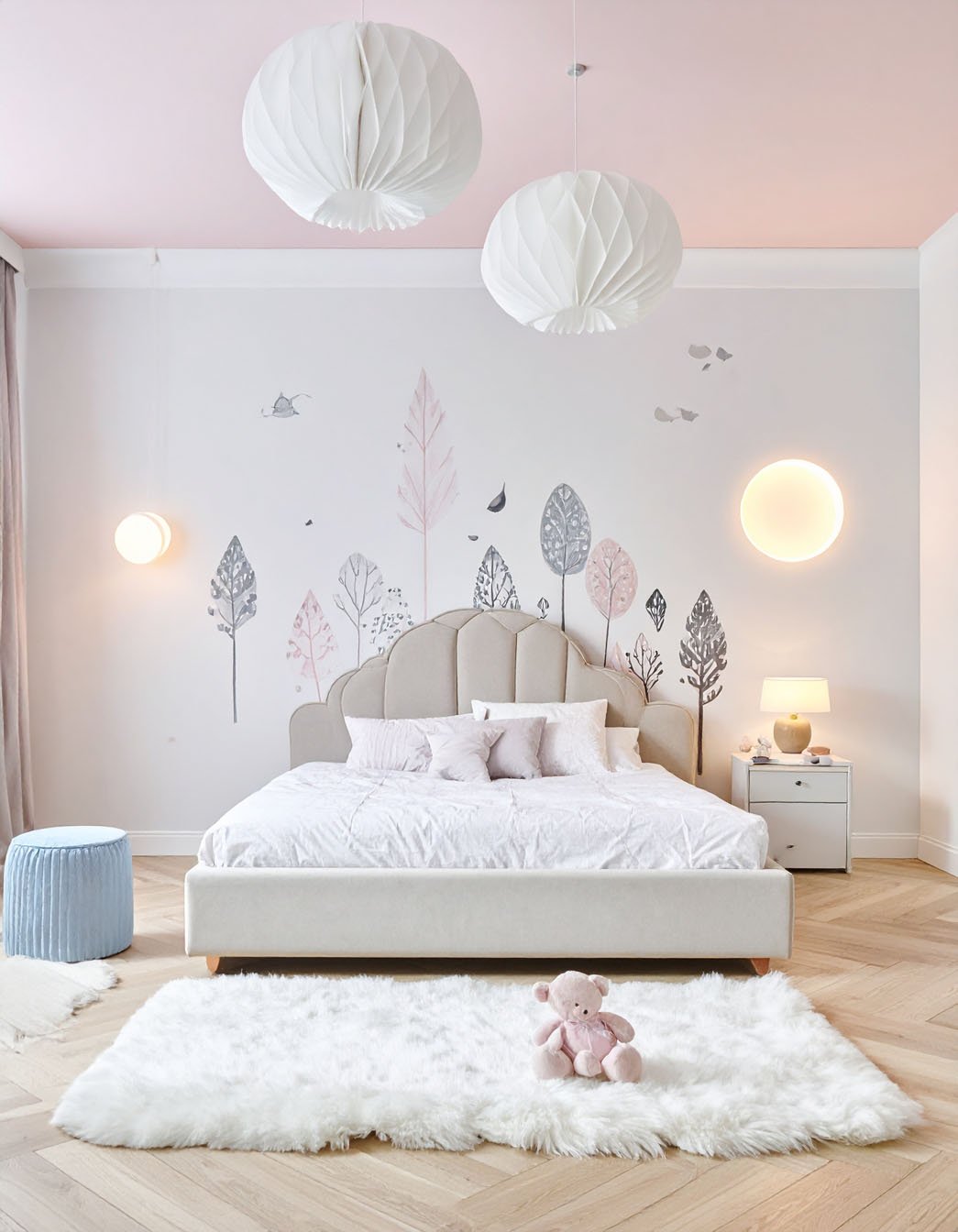 Chambre d'enfant avec lit à tête de lit festonnée beige, décorations murales d'arbres stylisés et suspensions en papier