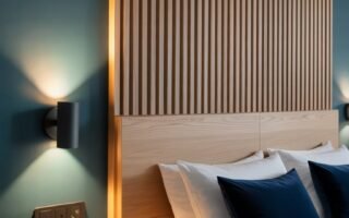 Tête de lit en tasseaux de bois clair intégrée avec chevets flottants sur un mur bleu